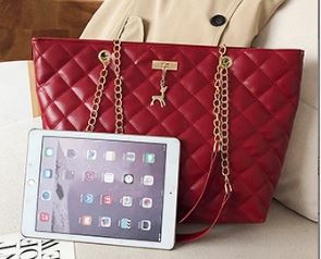 Image of a ladies red quilted pattern leather shoulder tote-bag sitting on a chair next to a cream colored jacket, i-pad, and a magazine.