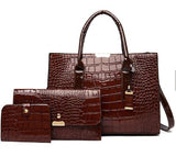 Image of a burgundy Alligator skin tote bag, clutch, and small wallet standing side by side