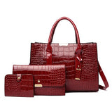 Image of a Alligator skin red tote bag, clutch, and small wallet standing side by side