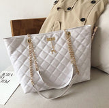 Image of a ladies white quilted pattern  leather shoulder tote-bag sitting on a chair next to a cream colored jacket and a magazine. 